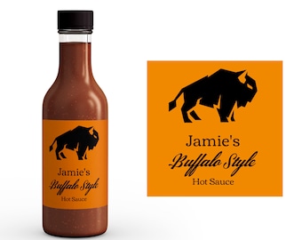 Könnte beinhalten: Eine Glasflasche Jamie's Buffalo Style Hot Sauce mit einer schwarzen Büffel-Silhouette auf dem Etikett. Das Etikett ist orange mit schwarzem Text.