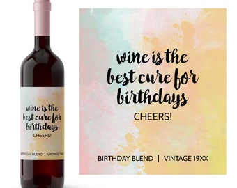 Puede incluir: Una botella de vino con una etiqueta que dice "wine is the best cure for birthdays CHEERS!" La etiqueta tiene un fondo de acuarela con tonos de rosa, amarillo y azul. La botella está etiquetada como "Birthday Blend | Vintage 19XX".