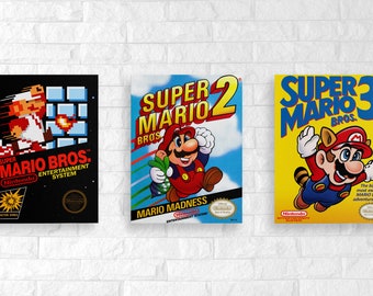 May include: Three vintage Super Mario Bros. video game cartridge covers. The first cover is black with a red and white Mario character running. The second cover is blue with a red and white Mario character jumping. The third cover is yellow with a red and white Mario character flying with a raccoon tail.