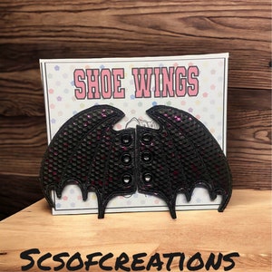 May include: Black and pink sequined shoe wings with a bat wing design. The wings have a textured surface and are attached with eyelets. The wings are displayed on a white card with the text "Shoe Wings" and "SCSOFCREATIONS".
