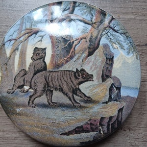 Puede incluir: Un plato de cerámica vintage con una ilustración detallada de dos zorros en un entorno de bosque. El plato presenta un esquema de color azul y verde con detalles intrincados de árboles, rocas y follaje.