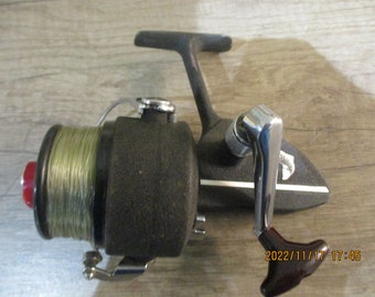 May include: A black fishing reel with a silver handle and a spool of green fishing line. The reel has a white stripe on the side.