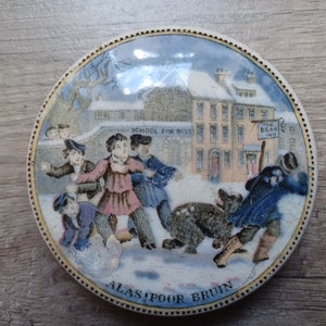 May include: A vintage ceramic lid featuring a colourful illustration of children playing in the snow outside a building with the text "School for Boys" and "The Bear Inn". The lid has a gold rim and the text "Alas, Poor Bruin" at the bottom.