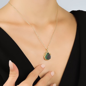 Pode incluir: Um colar de corrente de ouro com um pingente de pedra preciosa verde e vermelha. O pingente é engastado em uma moldura de ouro e tem a forma de uma lágrima.