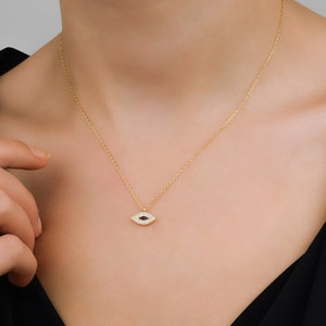 Può includere: Una collana con catena dorata con un piccolo ciondolo a forma di occhio turco. Il ciondolo è incastonato con pietre preziose trasparenti e blu.