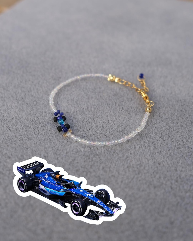 May include: A delicate bracelet featuring small, iridescent beads and a gold-colored chain. The bracelet includes a cluster of blue and black beads. A blue race car sticker is also present.