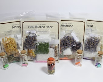 Può includere: Kit di vasetti di incantesimi fai-da-te con ingredienti per varie intenzioni. I kit sono etichettati "Money", "Heal Broken Heart", "Attraction" e "Sleep". Includono erbe, cristalli e piccoli vasetti di vetro con tappi di sughero.