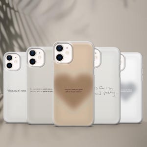May include: Five clear phone cases with different designs. One case has a blurred heart, another has the text "I love you, it's ruining", and others feature handwritten phrases. The cases are designed to fit a smartphone.