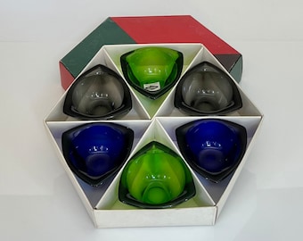 May include: A set of six glass shot glasses in a hexagonal box. The glasses are in shades of green, blue, and gray. The box is white with a green and red lid.