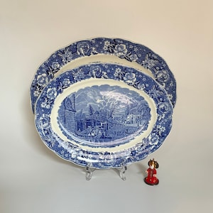 Könnte beinhalten: Zwei blaue und weiße ovale Keramikteller mit floralem Rand und einer Szene einer Stadt mit einer Brücke und Booten in der Mitte.