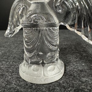 Puede incluir: Una figura de &aacute;ngel de cristal transparente con dise&ntilde;os detallados de alas y cuerpo. El &aacute;ngel tiene una superficie texturizada y est&aacute; sobre una base redonda. Las alas est&aacute;n extendidas y el cuerpo tiene un patr&oacute;n decorativo.