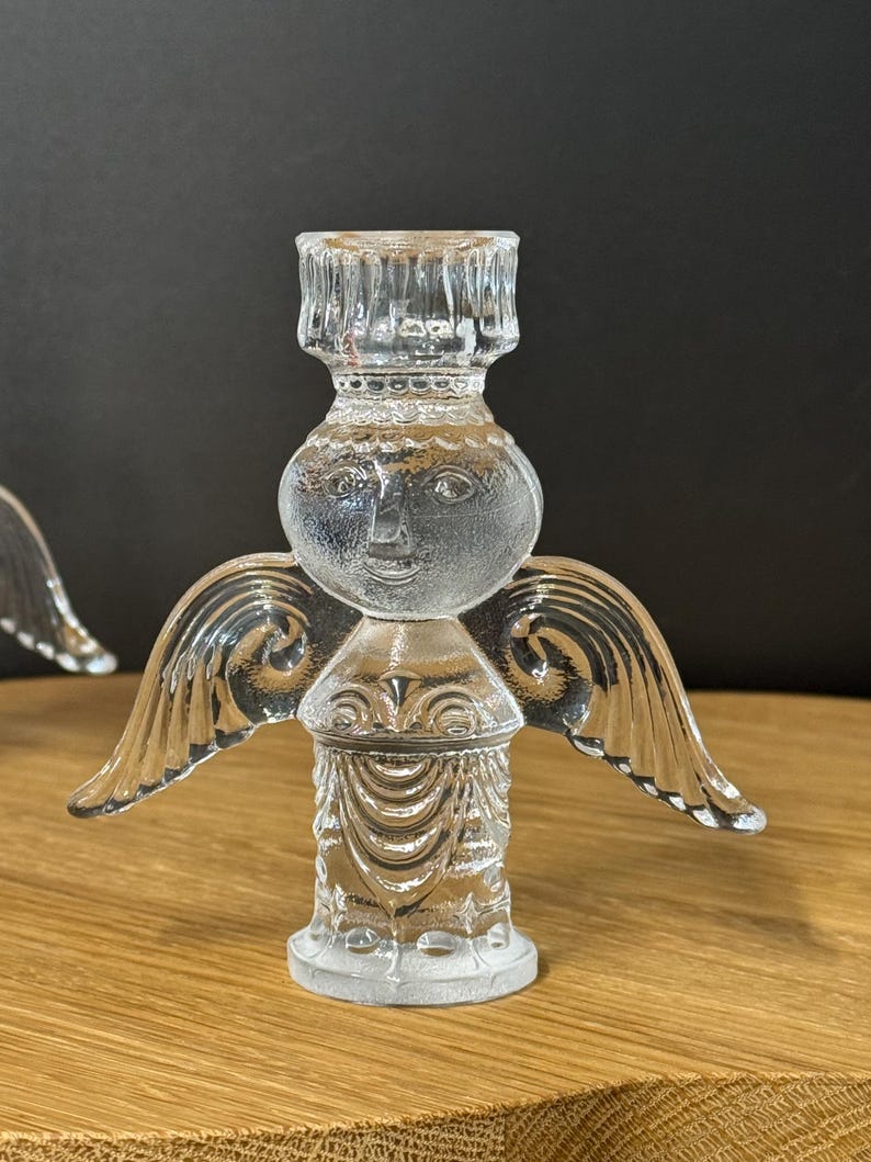 Puede incluir: Candelabro de &aacute;ngel de cristal transparente con alas detalladas y una cara sonriente. El candelabro tiene una base redonda y una parte superior cil&iacute;ndrica para sostener una vela. La figura del &aacute;ngel es de cristal transparente.