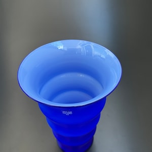 May include: A blue glass vase with a white interior and a rippled design. The vase is marked with the text "Holme Gaard 1825".