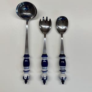 Puede incluir: Un juego de tres utensilios para servir: un cucharón, un tenedor para ensalada y una cuchara. Cada utensilio tiene una cabeza de acero inoxidable y un mango con un diseño de cerámica azul y blanco. Los mangos tienen forma bulbosa.
