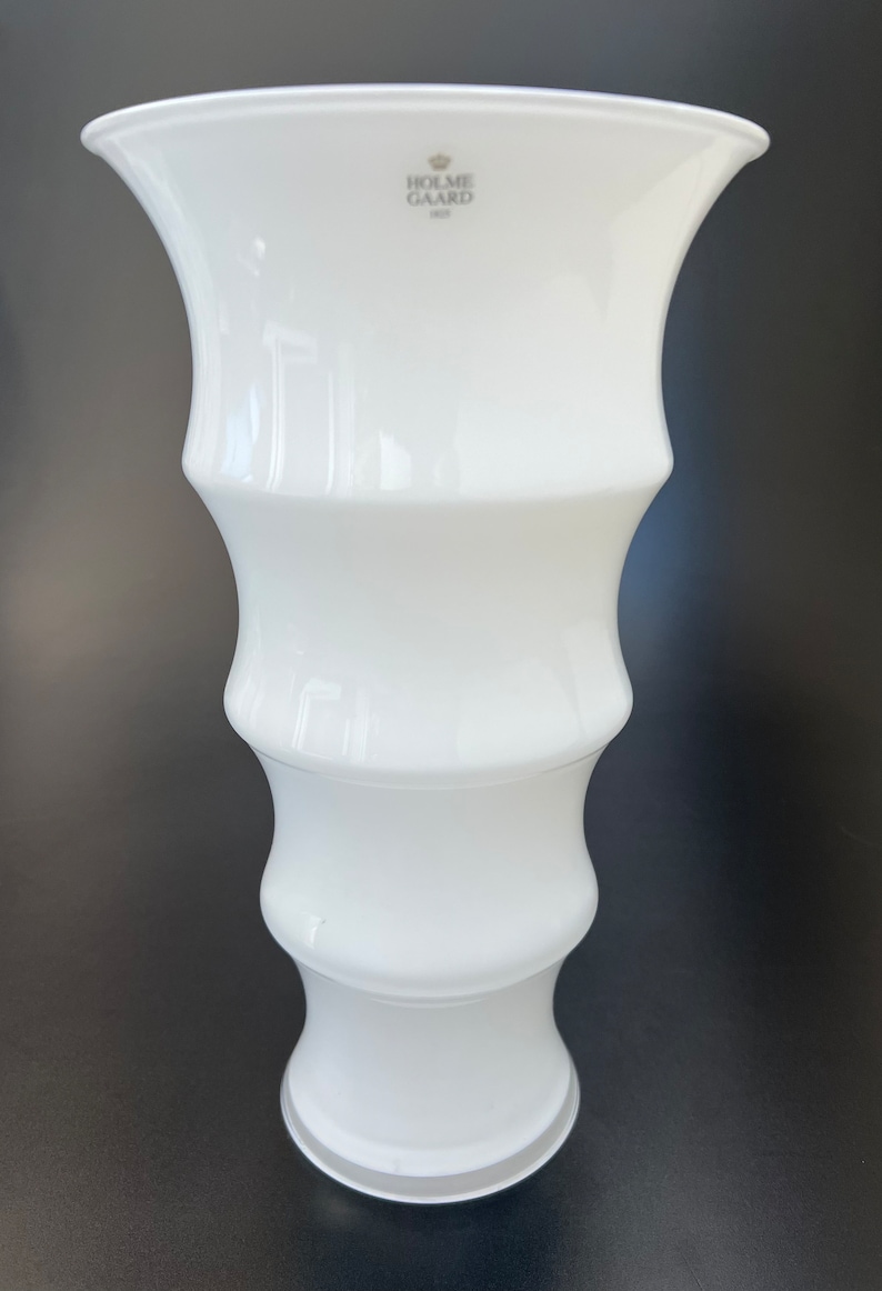 May include: White ceramic vase with a fluted design. The vase is marked with the logo "Holme Gaard 1825".