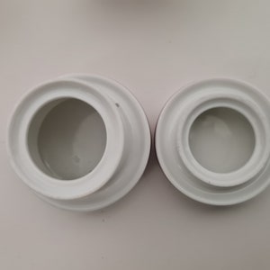 May include: Two white ceramic lids with a raised rim and a smooth, white interior. The lids are different sizes and are on a white background.