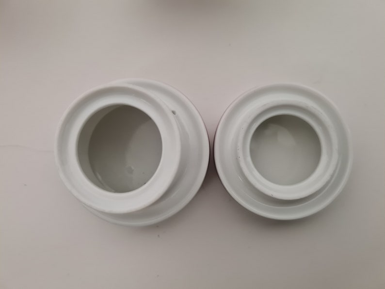May include: Two white ceramic lids with a raised rim and a smooth, white interior. The lids are different sizes and are on a white background.