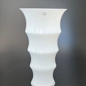 May include: White ceramic vase with a fluted design. The vase has a wide mouth and a narrow base. The vase is made by Holme Gaard, 1923.