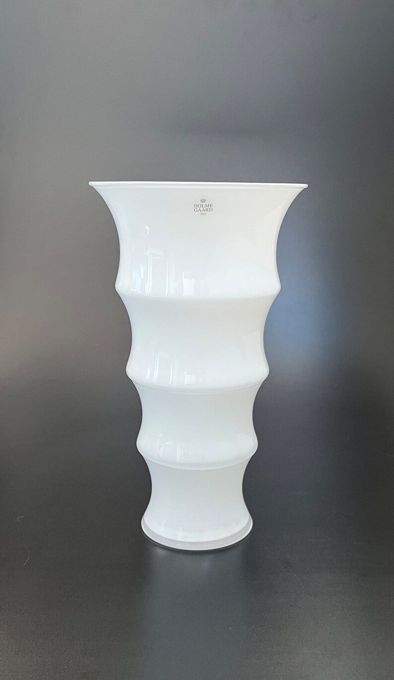 May include: White ceramic vase with a fluted design. The vase has a wide mouth and a narrow base. The vase is made by Holme Gaard, 1923.