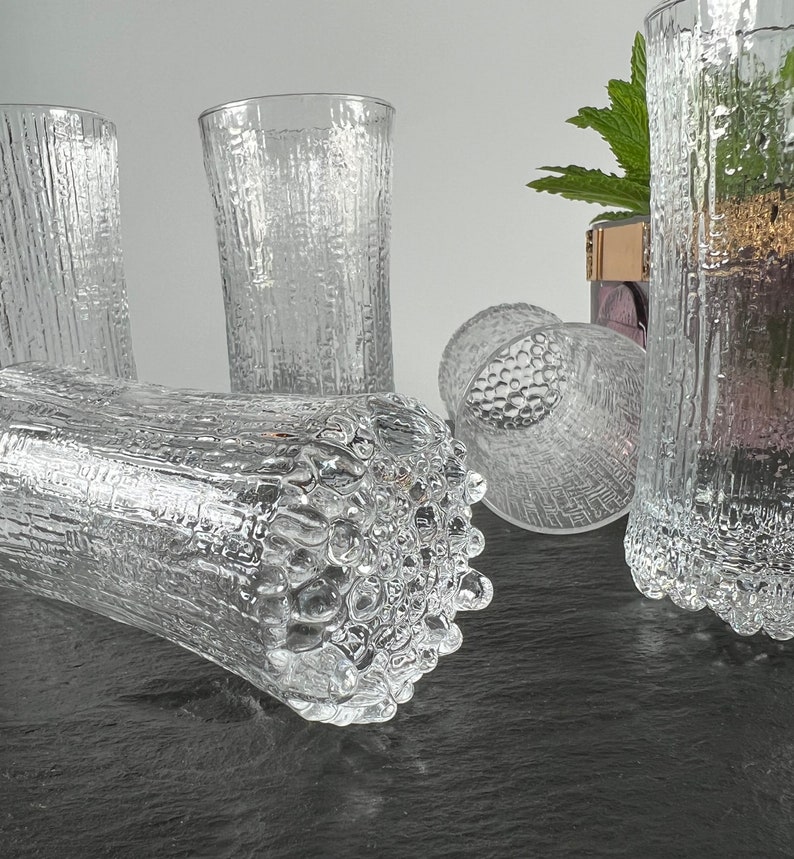 May include: Clear textured glass tumblers. The glasses have a bark-like texture on the exterior. One tumbler is lying on its side, while others stand upright. The glassware is suitable for water, juice, or other beverages.