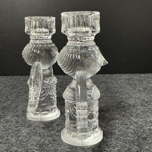 Puede incluir: Dos candelabros de vidrio transparente. Cada candelabro tiene forma de p&aacute;jaro con una base redonda, un cuerpo detallado y una parte superior cil&iacute;ndrica para sostener una vela. El vidrio tiene un dise&ntilde;o texturizado y detallado.