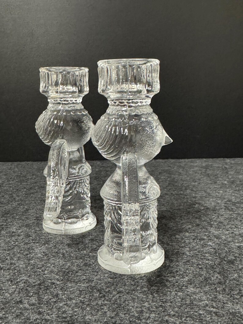 Puede incluir: Dos candelabros de vidrio transparente. Cada candelabro tiene forma de p&aacute;jaro con una base redonda, un cuerpo detallado y una parte superior cil&iacute;ndrica para sostener una vela. El vidrio tiene un dise&ntilde;o texturizado y detallado.