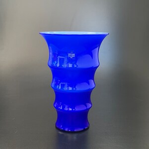May include: A cobalt blue glass vase with a flared top and a rippled design. The vase is marked with the text "Holme Gard" in white.