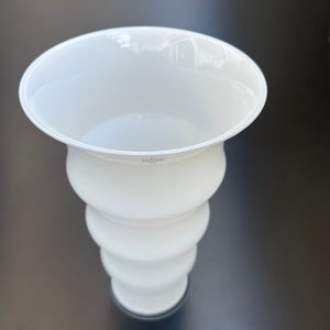 May include: White ceramic vase with a flared top and a rounded, wavy body. The vase has a black base.