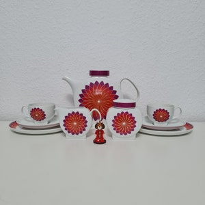 May include: A white tea set with a red and purple floral design. The set includes a teapot, creamer, sugar bowl, two cups, and two saucers.