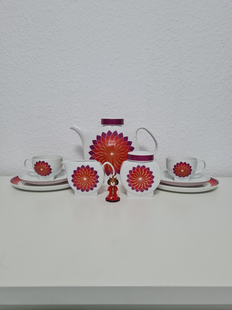 May include: A white tea set with a red and purple floral design. The set includes a teapot, creamer, sugar bowl, two cups, and two saucers.