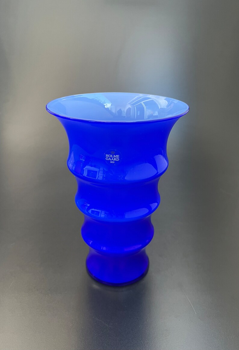 May include: A cobalt blue glass vase with a wavy design. The vase is made by Holme Gard, a Danish company founded in 1825.