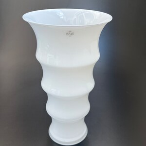 May include: White ceramic vase with a wavy design and a logo that reads "Holme Gard 1923".