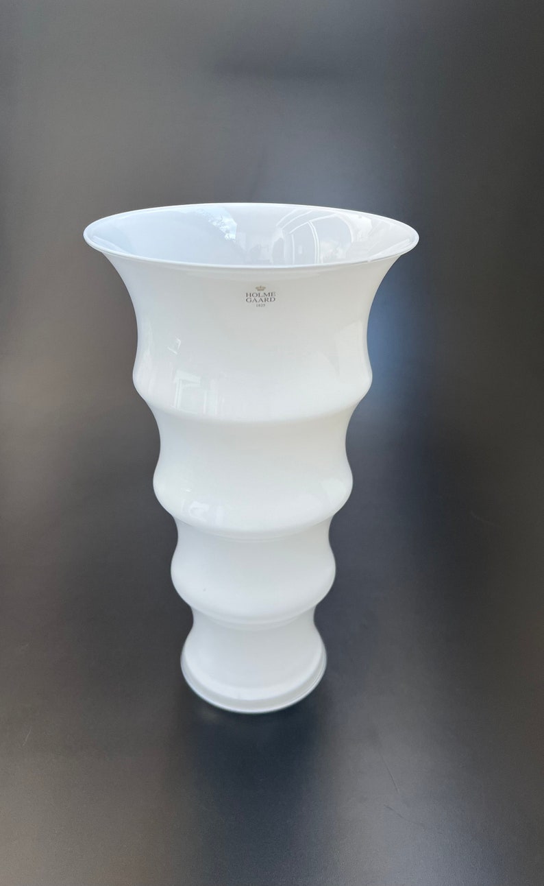 May include: White ceramic vase with a wavy design and a logo that reads "Holme Gard 1923".