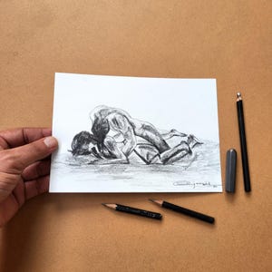 May include: A charcoal drawing on white paper depicting two figures in an intimate embrace. The artwork features shaded contours and expressive lines, with a signature in the bottom right corner. Three black pencils and an eraser are placed nearby.