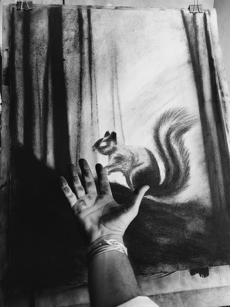 May include: A charcoal drawing on paper depicting a squirrel in a forest setting with tall, dark vertical tree trunks. The artwork uses high-contrast black and white shading to create depth, with the squirrel positioned centrally in the composition.