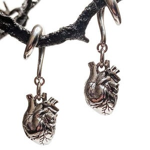 Può includere: Un paio di orecchini pendenti a forma di cuore anatomico in argento. Ogni orecchino presenta un ciondolo a forma di cuore anatomico dettagliato appeso a un cerchio d'argento.