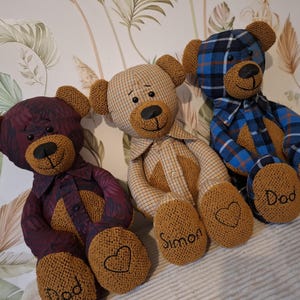 May include: Three fabric teddy bears with embroidered features. Each bear wears a shirt in a different pattern: burgundy, tan, and blue plaid. The bears have embroidered hearts and names on their feet. The bears are handmade.