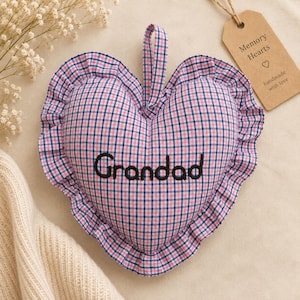 Op de afbeelding: Een hartvormig stoffen ornament met een roze en marineblauw gingham ruitpatroon, een geplooide rand en een stoffen ophanglus. Het woord Grandad is in zwart garen in het midden geborduurd. Een bruin papieren label bevat de tekst Memory Hearts.