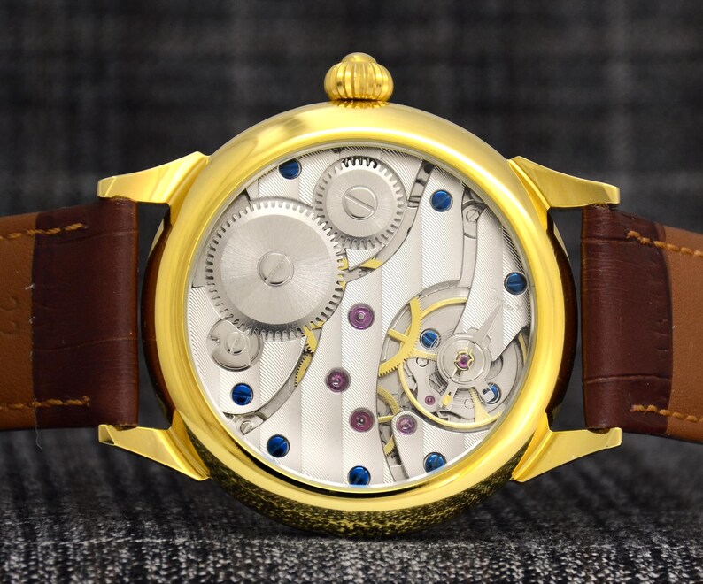 May include: A gold-toned wristwatch with a brown leather band. The watch face reveals intricate mechanical components, including gears, screws, and jewels. The watch has a round face and a textured, striped background.