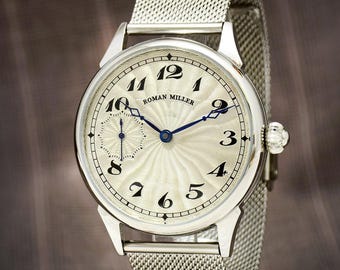 May include: A silver Roman Miller wristwatch with a white face and blue hands. The watch has a unique design with a sunburst pattern and Roman numeral hour markers.