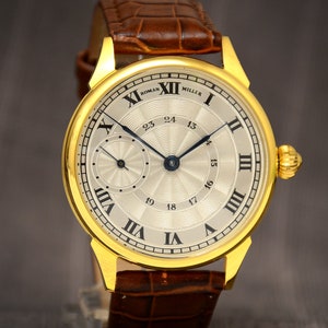 May include: A gold-toned wristwatch with a light-colored face and black hands. The watch features Roman numerals and the text "ROMAN MILLER". The watch has a brown leather band.