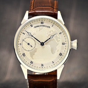 May include: A silver Roman Miller wristwatch with a white face and black hands. The face features a world map design with a smaller subdial at the 3 o'clock position. The watch has a brown leather strap.
