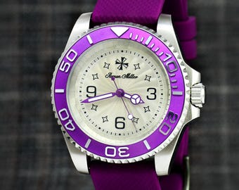Può includere: Un orologio da polso con cassa color argento e cinturino in silicone viola vivace. Il quadrante presenta un motivo a onde testurizzato, la scritta Roman Miller, indici a forma di stella e numeri a ore tre, sei e nove. Una lunetta viola circonda il quadrante.