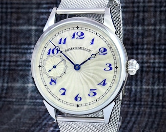 May include: A silver-tone wristwatch with a cream-colored dial featuring a wavy guilloche pattern, blue Arabic numerals, and the text ROMAN MILLER. The watch has blue hands, a small sub-dial, and a silver-tone stainless steel mesh strap.