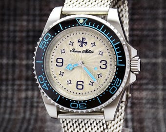 Può includere: Un orologio da polso argentato con cinturino a maglia e lunetta girevole nera e blu. Il quadrante è argento chiaro con lancette e numeri blu. Il quadrante ha il testo "Roman Miller".