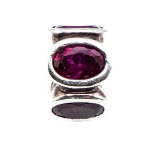 May include: A silver charm with three dark purple oval-shaped gemstones. The charm has a polished finish and is set against a white background. The gemstones are a deep, rich color.