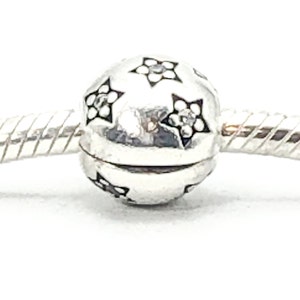 Puede incluir: Un brazalete de plata con un abalorio de plata en forma de perla con un diseño de estrella negra.
