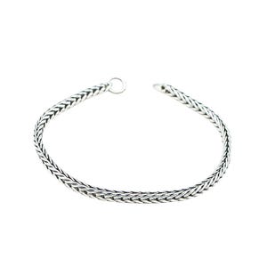 Puede incluir: Un brazalete plateado con un diseño de cadena trenzada. El brazalete está abierto en un extremo y tiene un pequeño lazo en el otro. El brazalete está sobre un fondo blanco.