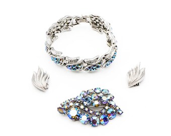 Op de afbeelding: Een vintage sieradenset bestaande uit een zilveren armband, een broche en een paar oorbellen. De sieraden zijn versierd met iriserende blauwe strass.
