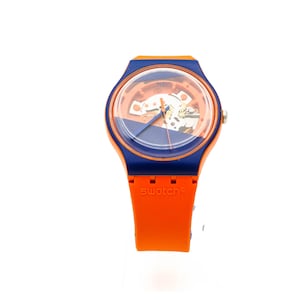 May include: A blue and orange Swatch watch with a skeletonized dial. The watch has a blue face with a clear window revealing the inner workings of the watch. The watch has an orange band with the word "swatch" printed on it.